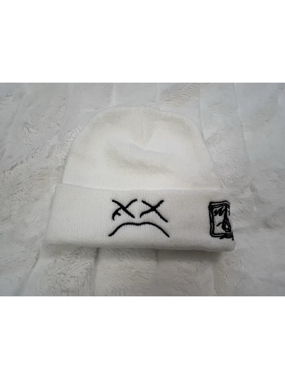White KAWS beanie with black embroidered sad face and box logo